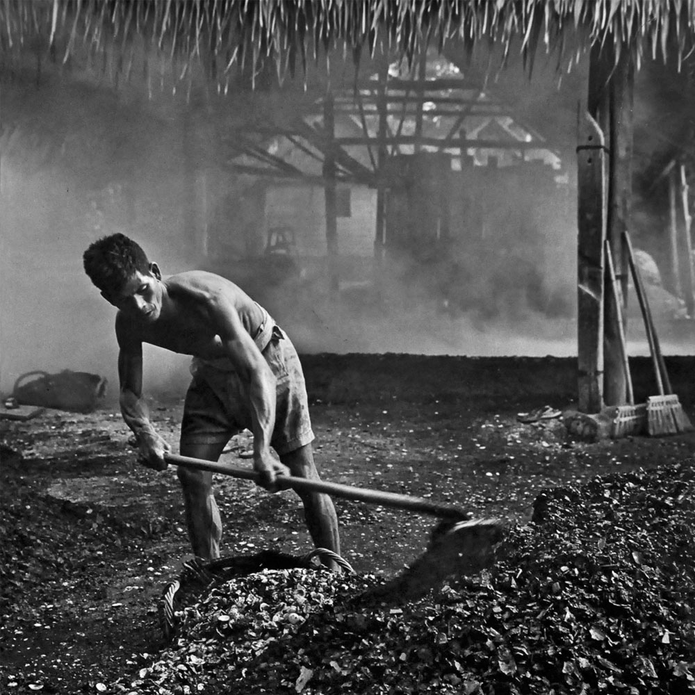 Passing Time by Lui Hock Seng - Man shovelling crushed cockle shells to make whitewash paint, Tanah Merah, c. 1960s – 1970s
