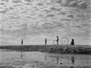 Passing Time by Lui Hock Seng - Kids playing with bicycle wheel rims, Bedok Beach, c. 1960s – 1970s